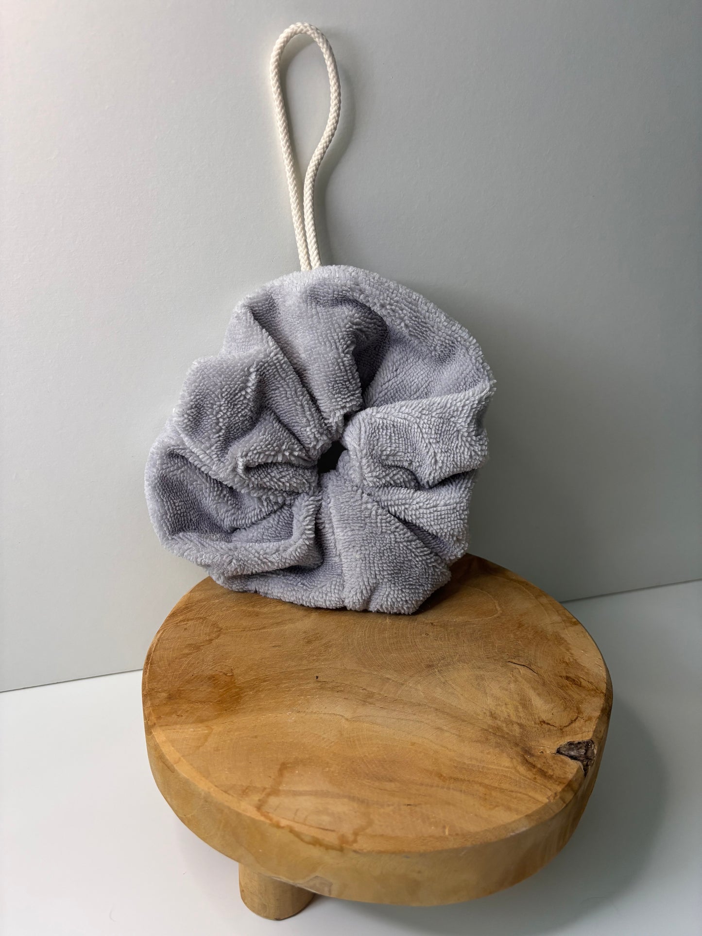 Fleur de douche en éponge de bambou de couleur grise, posée sur une surface en bois
