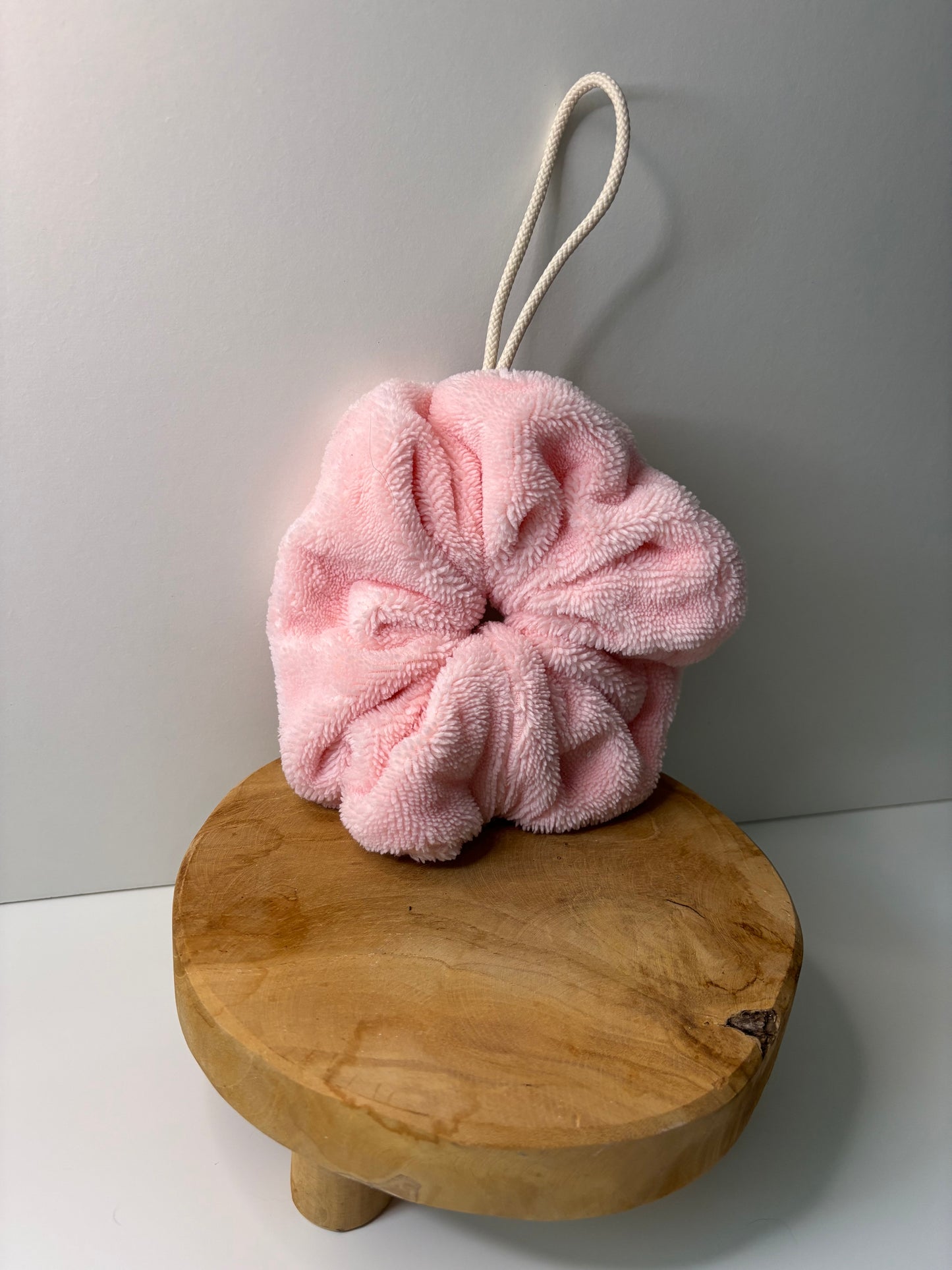 Fleur de douche en éponge de bambou de couleur rose, posée sur une surface en bois