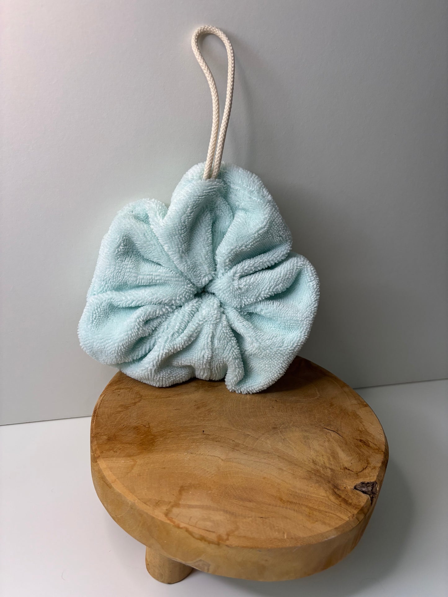 Fleur de douche en éponge de bambou de couleur vert d'eau, posée sur une surface en bois