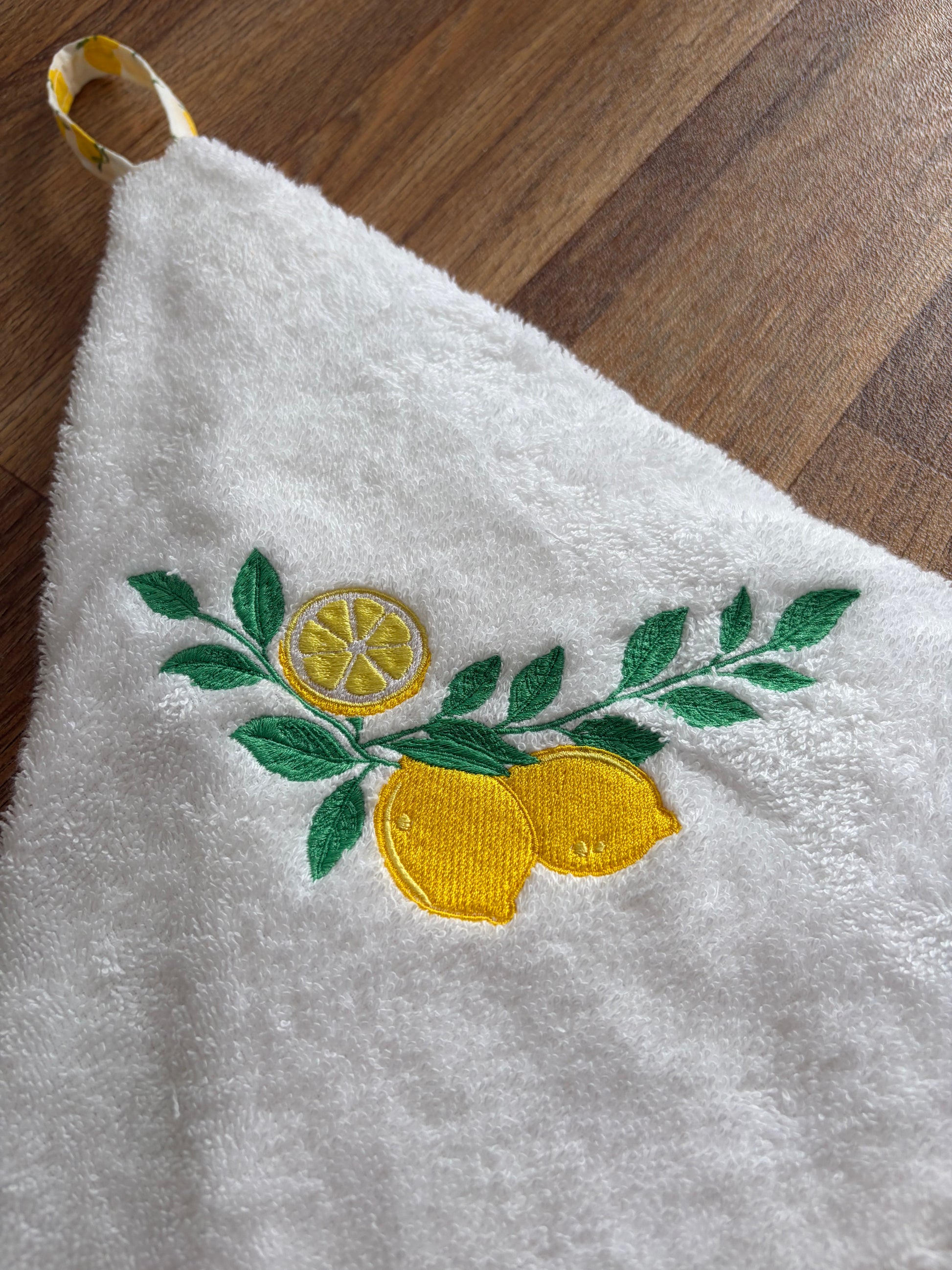 Détail des citrons jaunes et du feuillage vert brodés sur l’éponge blanche de l’essuie-mains