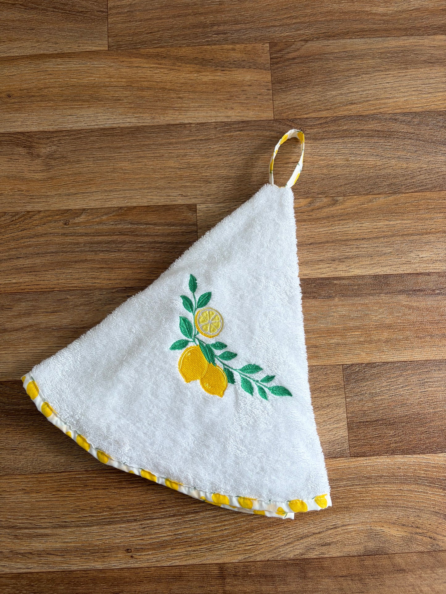 Essuie-mains rond blanc brodé de citrons jaunes et de feuilles vertes, avec bordure et attache imprimées de citrons