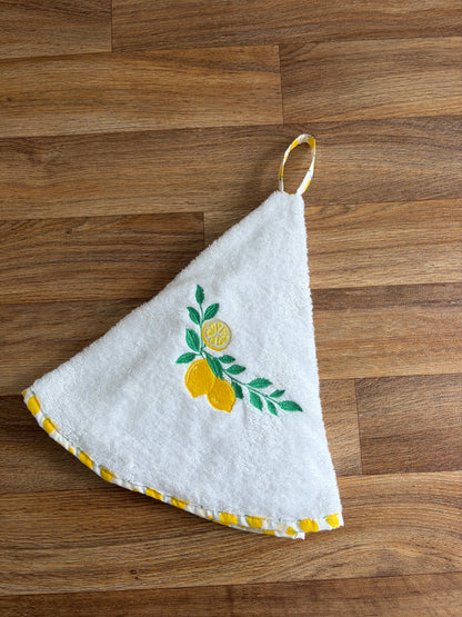 Essuie-mains rond blanc brodé de citrons jaunes et de feuilles vertes, avec bordure et attache imprimées de citrons