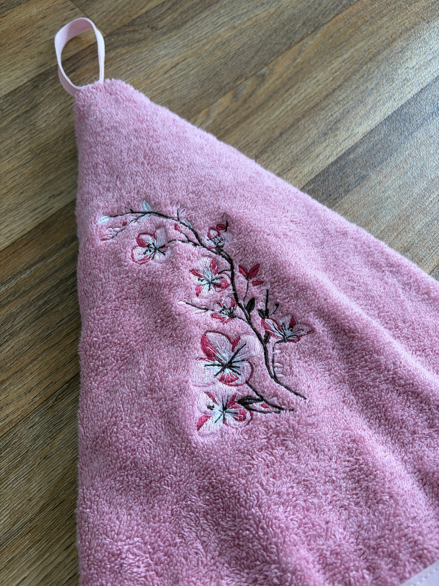 Gros plan sur les fleurs de cerisier brodées en rose et blanc sur l’essuie-mains en éponge rose
