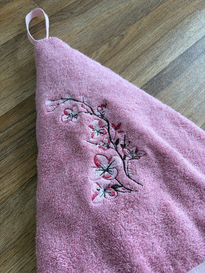 Gros plan sur les fleurs de cerisier brodées en rose et blanc sur l’essuie-mains en éponge rose