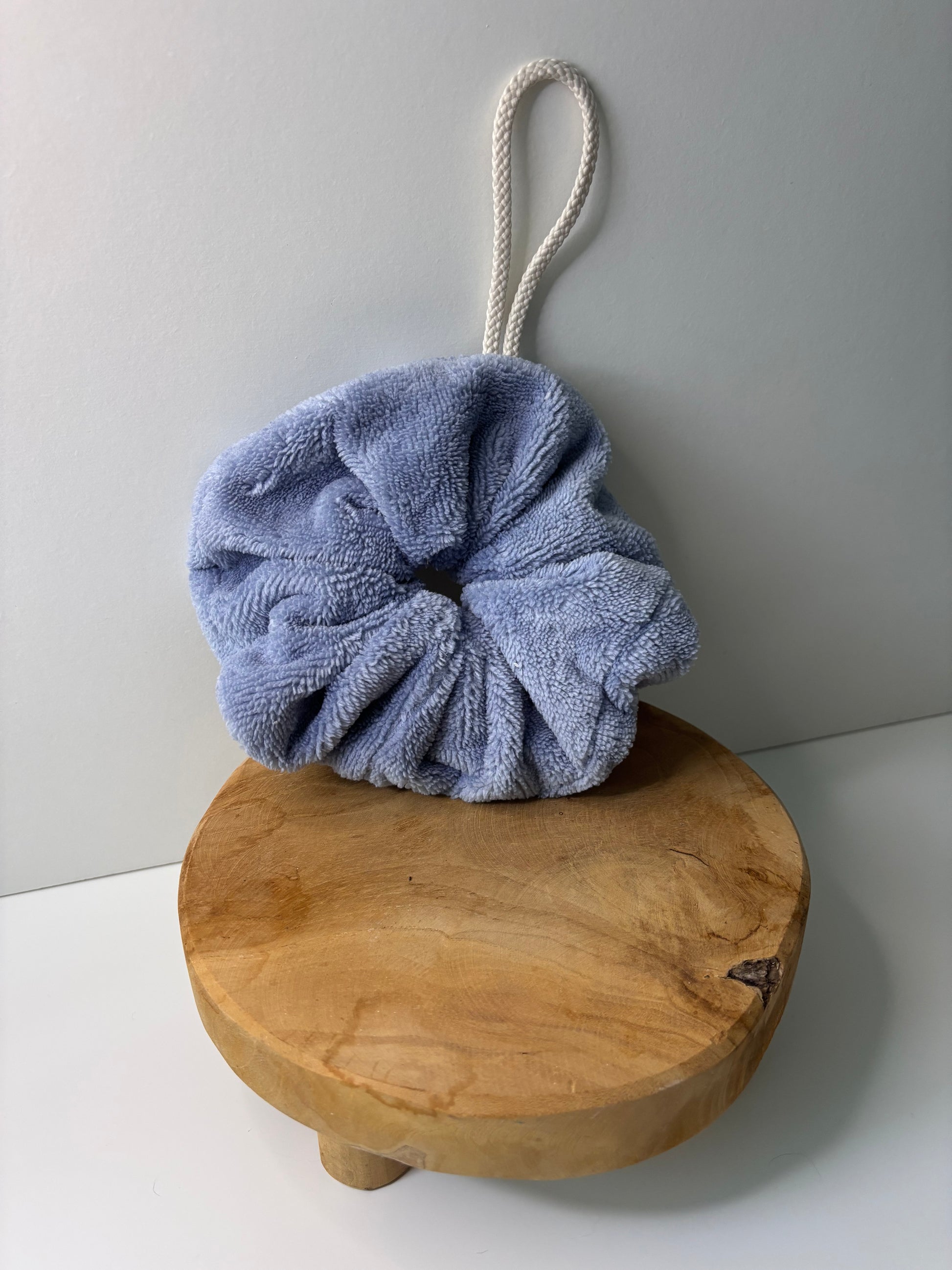 Fleur de douche en éponge de bambou de couleur bleu, posée sur une surface en bois