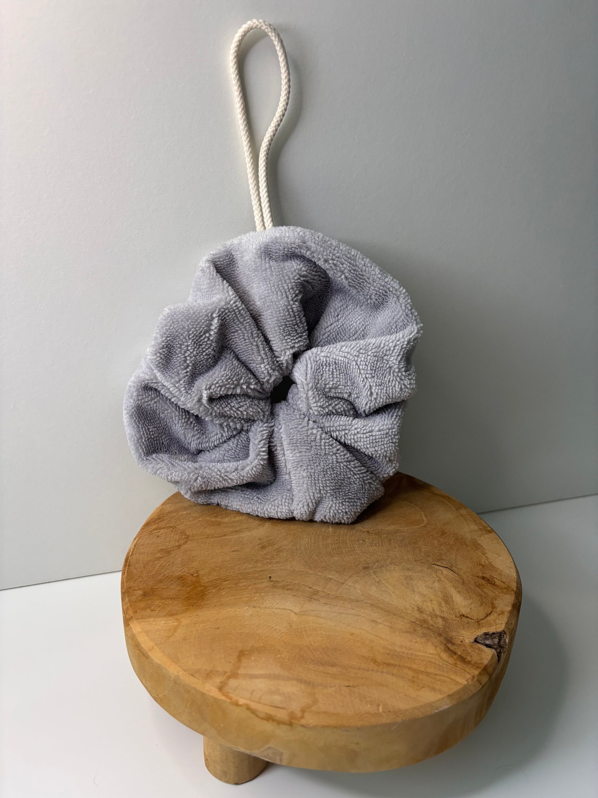 Fleur de douche en éponge de bambou de couleur grise, posée sur une surface en bois