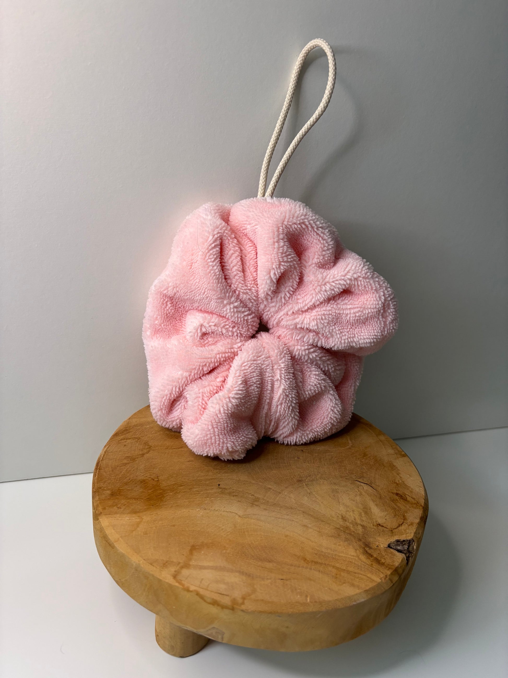 Fleur de douche en éponge de bambou de couleur rose, posée sur une surface en bois